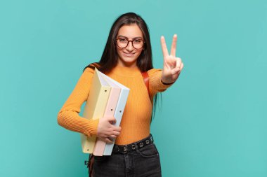Genç ve güzel bir kadın gülümsüyor ve mutlu görünüyor, kaygısız ve pozitif, tek elle zafer ya da barış işareti yapıyor. öğrenci konsepti