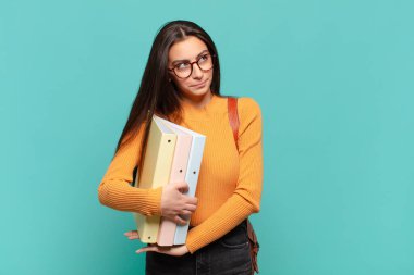 Genç, güzel bir kadın omuz silkiyor, kafası karışık ve kararsız, kolları bağlı ve şaşkın görünüyor. öğrenci konsepti