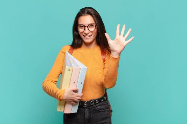Genç ve güzel bir bayan gülümsüyor ve arkadaş canlısı görünüyor. Beş ya da beş numarayı gösteriyor. Elleri önde ve geri sayıyor. öğrenci konsepti