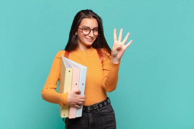 Genç, güzel bir bayan gülümsüyor ve arkadaş canlısı görünüyor. Dört ya da dört numarayı gösteriyor. Elleri önde ve geri sayıyor. öğrenci konsepti