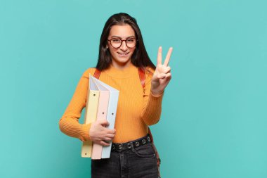 Genç, güzel bir kadın gülümsüyor ve arkadaş canlısı görünüyor. İki ya da iki numarayı gösteriyor. Elleri önde, geriye doğru sayıyor. öğrenci konsepti