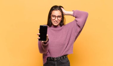 Genç, güzel bir kadın kendini stresli, endişeli, endişeli ya da korkmuş hissediyor. Elleri başının üstünde, hatayla panikliyor. telefon ekranı kavramı