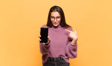 Genç, güzel bir kadın mutlu, şaşırmış ve gururlu hissediyor. Heyecanlı ve şaşkın bir bakışla kendini işaret ediyor. telefon ekranı kavramı
