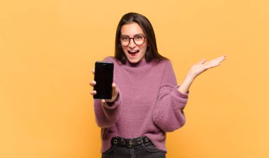 Genç, güzel bir kadın mutlu, heyecanlı, şaşırmış ya da şok olmuş hissediyor. İnanılmaz bir şeye gülümsüyor ve hayrete düşüyor. telefon ekranı kavramı