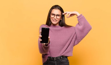 Genç, güzel bir kadın kafası karışık ve şaşkın hissediyor. Deli, deli ya da aklını kaçırmış olduğunu gösteriyor. telefon ekranı kavramı