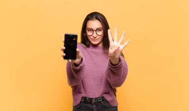 Genç, güzel bir bayan gülümsüyor ve arkadaş canlısı görünüyor. Dört ya da dört numarayı gösteriyor. Elleri önde ve geri sayıyor. telefon ekranı kavramı