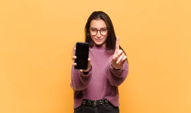 Genç ve güzel bir kadın gülümsüyor ve arkadaş canlısı görünüyor. Bir numarayı gösteriyor ya da ilk eli önde, geri sayıyor. telefon ekranı kavramı