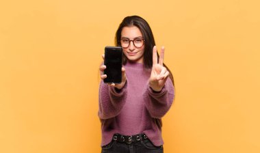 Genç, güzel bir kadın gülümsüyor ve arkadaş canlısı görünüyor. İki ya da iki numarayı gösteriyor. Elleri önde, geriye doğru sayıyor. telefon ekranı kavramı