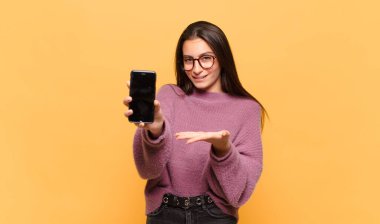 Genç, güzel bir kadın neşeyle gülümsüyor, mutlu hissediyor ve fotokopi uzayda avucuyla bir konsept gösteriyor. telefon ekranı kavramı