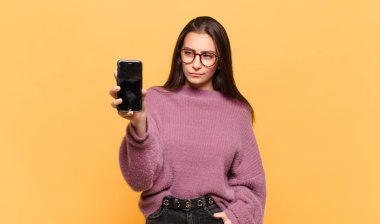 Genç, güzel bir kadın üzgün, üzgün ya da kızgın. Olumsuz bir tavırla yan yana bakıyor, anlaşmazlık içinde kaşlarını çatıyor. telefon ekranı kavramı