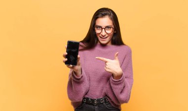 Genç ve güzel bir kadın heyecanlı ve şaşırmış görünüyor. Yana ve yukarı doğru uzayı işaret ediyor. telefon ekranı kavramı