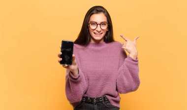 Genç, güzel bir kadın, kendine güvenerek gülümsüyor. Geniş bir gülümseme, pozitif, rahat, tatmin olmuş bir tavır sergiliyor. telefon ekranı kavramı