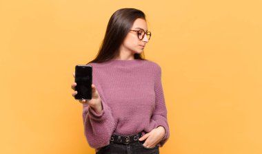 Profil görünümünde genç ve güzel bir kadın uzayı kopyalamaya çalışıyor. Düşünüyor, hayal ediyor ya da hayal kuruyor. telefon ekranı kavramı