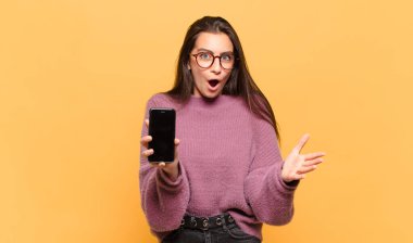 Genç ve güzel bir kadın ağzı açık ve şaşırmış, şok olmuş ve hayrete düşmüş inanılmaz bir sürprizle. telefon ekranı kavramı