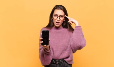 Genç, güzel bir kadın şaşırmış, ağzı açık, şok olmuş, yeni bir düşünce, fikir ya da konsept keşfediyor. telefon ekranı kavramı