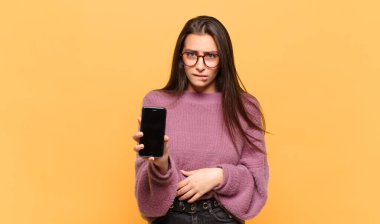 Kafası karışmış ve kafası karışmış genç bir kadın gergin bir hareketle dudağını ısırıyor, sorunun cevabını bilmiyor. telefon ekranı kavramı