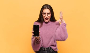 Genç ve güzel bir kadın ellerini havaya kaldırıp bağırıyor. Öfkeli, sinirli, stresli ve üzgün hissediyor. telefon ekranı kavramı