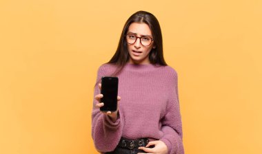 young pretty woman feeling puzzled and confused, with a dumb, stunned expression looking at something unexpected. phone screen concept