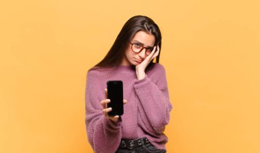 Genç ve güzel bir kadın yorgun, sıkıcı ve can sıkıcı bir işten sonra sıkılmış, hayal kırıklığına uğramış ve uykulu hissediyor, el ele tutuşarak. telefon ekranı kavramı