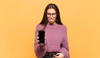 Genç ve güzel bir kadın iğrenmiş ve rahatsız olmuş hissediyor. Dilini dışarı çıkarıyor. Çirkin ve iğrenç şeylerden hoşlanmıyor. telefon ekranı kavramı