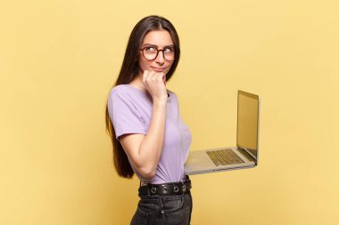 Genç, güzel bir kadın, mutlu, kendinden emin bir ifadeyle gülümsüyor, elleri çenesinde, merak ediyor ve yan tarafa bakıyor. dizüstü bilgisayar