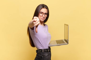Genç, güzel bir kadın kızgın, sinirli, hayal kırıklığına uğramış ya da hoşnutsuz, ciddi bir bakışla baş parmağını aşağı gösteren. dizüstü bilgisayar