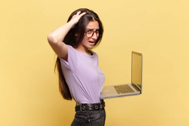 Genç, güzel bir kadın kendini stresli, endişeli, endişeli ya da korkmuş hissediyor. Elleri başının üstünde, hatayla panikliyor. dizüstü bilgisayar