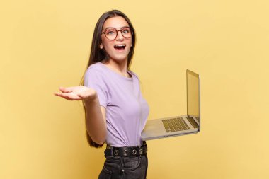 Genç, güzel bir kadın mutlu, heyecanlı, şaşırmış ya da şok olmuş hissediyor. İnanılmaz bir şeye gülümsüyor ve hayrete düşüyor. dizüstü bilgisayar