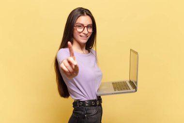 Genç ve güzel bir kadın gururla gülümsüyor ve gururla bir numaralı pozunu veriyor, bir lider gibi hissediyor. dizüstü bilgisayar