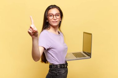 Genç ve güzel bir kadın gülümsüyor ve arkadaş canlısı görünüyor. Bir numarayı gösteriyor ya da ilk eli önde, geri sayıyor. dizüstü bilgisayar