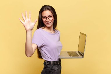 Genç ve güzel bir bayan gülümsüyor ve arkadaş canlısı görünüyor. Beş ya da beş numarayı gösteriyor. Elleri önde ve geri sayıyor. dizüstü bilgisayar