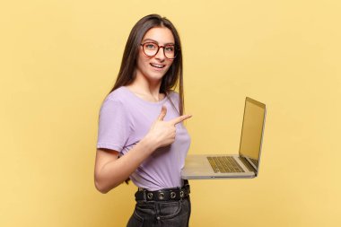 Genç ve güzel bir kadın heyecanlı ve şaşırmış görünüyor. Yana ve yukarı doğru uzayı işaret ediyor. dizüstü bilgisayar