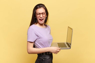 Genç ve güzel bir kadın agresif bir şekilde bağırıyor. Kızgın, sinirli ya da sinirli görünüyor. Hayır diye bağırıyor. dizüstü bilgisayar