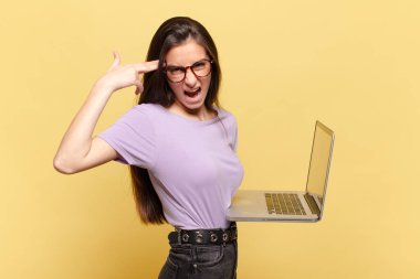 Genç ve güzel bir kadın mutsuz ve stresli görünüyor, intihar jesti, silahla işaret ediyor, kafasını işaret ediyor. dizüstü bilgisayar