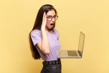 Genç, güzel bir kadın mutlu, heyecanlı ve şaşırmış hissediyor. İki eli de suratında yana bakıyor. dizüstü bilgisayar