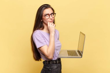 Genç, güzel bir kadın düşünüyor, kuşkulu ve şaşkın hissediyor, farklı seçeneklerle, hangi kararı vereceğini merak ediyor. dizüstü bilgisayar