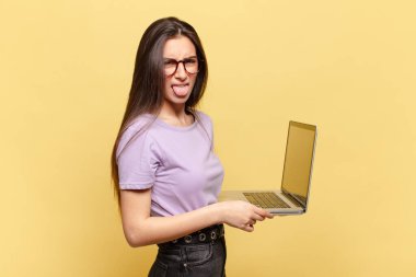 Genç ve güzel bir kadın iğrenmiş ve rahatsız olmuş hissediyor. Dilini dışarı çıkarıyor. Çirkin ve iğrenç şeylerden hoşlanmıyor. dizüstü bilgisayar