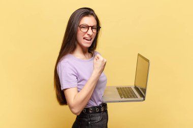 Genç ve güzel bir kadın öfkeli bir ifadeyle ya da yumruklarıyla başarıyı kutlarken agresif bir şekilde bağırıyor. dizüstü bilgisayar