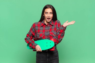 Genç ve güzel bir kadın şaşkın ve şaşkın hissediyor, şüpheci, farklı seçenekleri tartıyor ya da komik bir ifadeyle seçiyor. kaykay konsepti