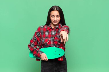 Genç ve güzel bir kadın kameraya bakıyor. Tatmin olmuş, kendinden emin, dostane bir gülümsemeyle. Seni seçiyor. kaykay konsepti