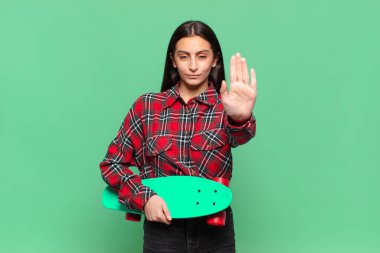 Genç ve güzel bir kadın ciddi, sert, hoşnutsuz ve kızgın görünüyor. kaykay konsepti