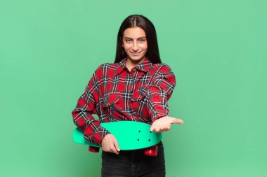 Genç, güzel bir kadın mutlu bir şekilde gülümsüyor. Dost canlısı, kendine güvenen, olumlu bakışlı, bir nesne ya da konsept sunuyor. kaykay konsepti