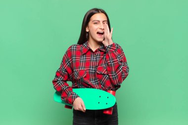 Genç, güzel bir kadın mutlu, heyecanlı ve pozitif hissediyor. Elleri ağızda, bağırarak bağırıyor. kaykay konsepti