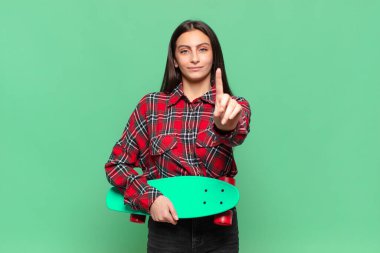 Genç ve güzel bir kadın gülümsüyor ve arkadaş canlısı görünüyor. Bir numarayı gösteriyor ya da ilk eli önde, geri sayıyor. kaykay konsepti