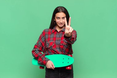 Genç, güzel bir kadın gülümsüyor ve arkadaş canlısı görünüyor. İki ya da iki numarayı gösteriyor. Elleri önde, geriye doğru sayıyor. kaykay konsepti