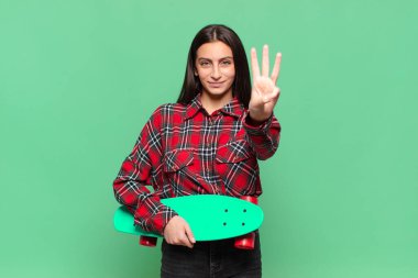 Genç, güzel bir bayan gülümsüyor ve arkadaş canlısı görünüyor. Üç ya da üç numarayı gösteriyor. Elleri önde, geriye doğru sayıyor. kaykay konsepti