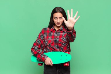 Genç ve güzel bir bayan gülümsüyor ve arkadaş canlısı görünüyor. Beş ya da beş numarayı gösteriyor. Elleri önde ve geri sayıyor. kaykay konsepti