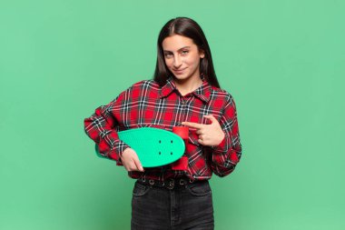 Genç, güzel bir kadın neşeyle gülümsüyor, mutlu hissediyor ve yan ve yukarı doğru işaret ediyor, fotokopi uzayında nesneler gösteriyor. kaykay konsepti