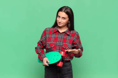 Genç, güzel bir kadın neşeyle gülümsüyor, mutlu hissediyor ve fotokopi uzayda avucuyla bir konsept gösteriyor. kaykay konsepti