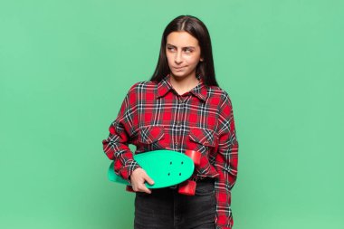 Genç, güzel bir kadın üzgün, üzgün ya da kızgın. Olumsuz bir tavırla yan yana bakıyor, anlaşmazlık içinde kaşlarını çatıyor. kaykay konsepti